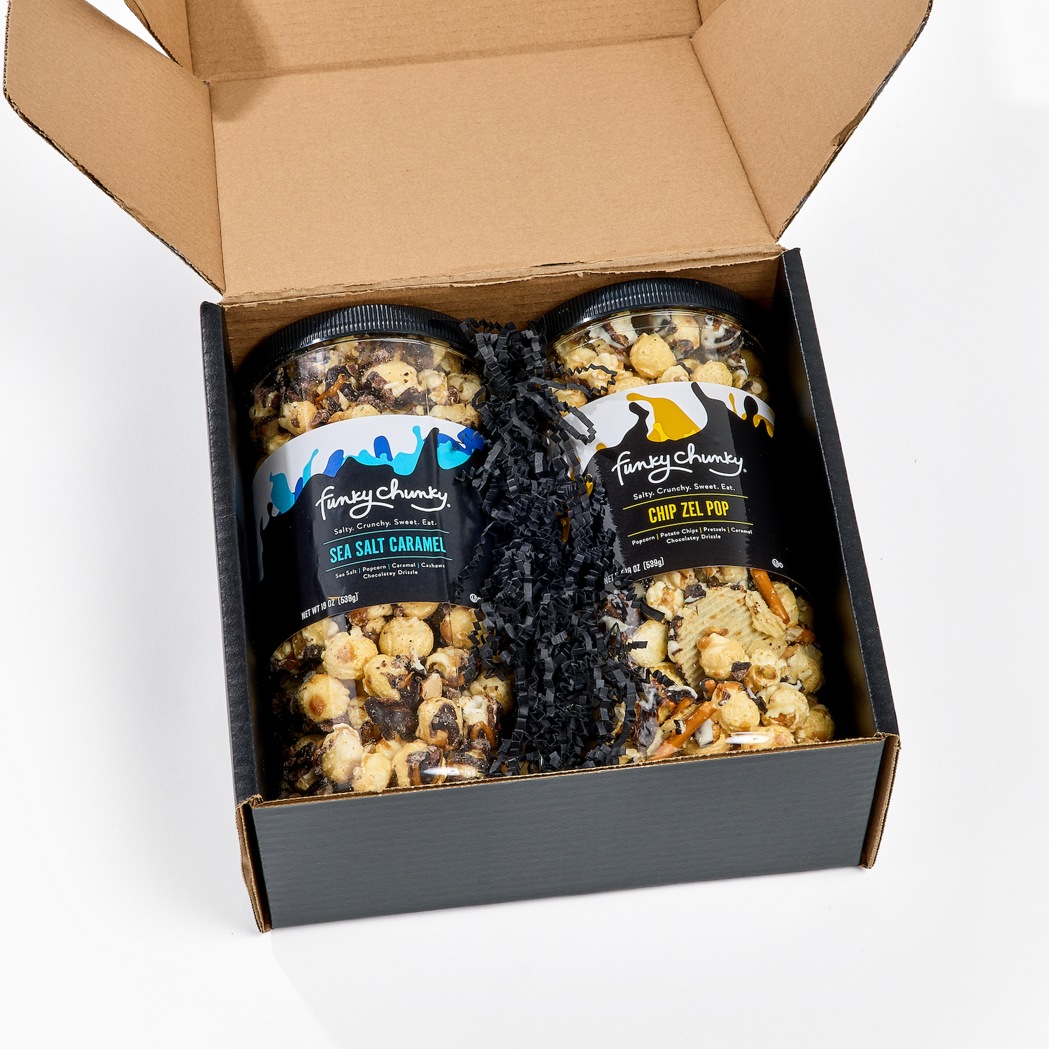 An open black gift box containing two jars of Funky
Chunky Sea Salt Caramel and Chip Zel Pop Gourmet Popcorns with a black ribbon on a white background.
